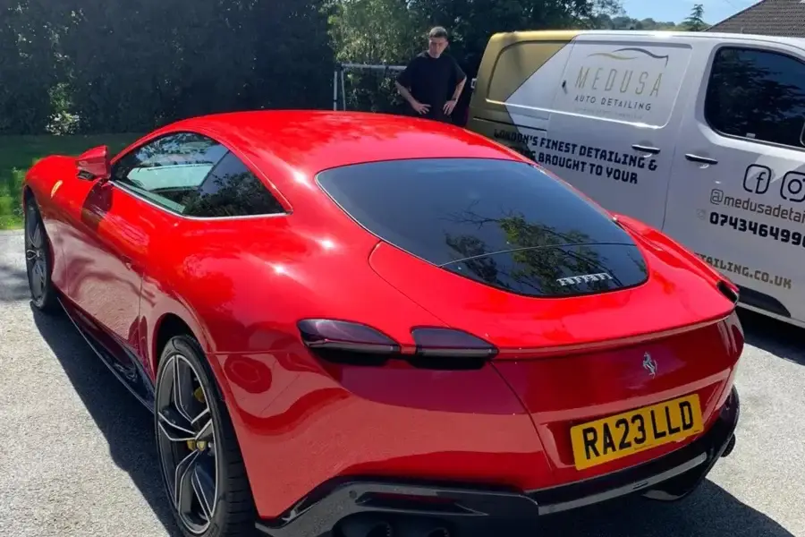 Rear view of a gleaming red Ferrari with RA23 LLD plate, freshly detailed by Medusa Auto Detailing, with branded van and detailer in background.